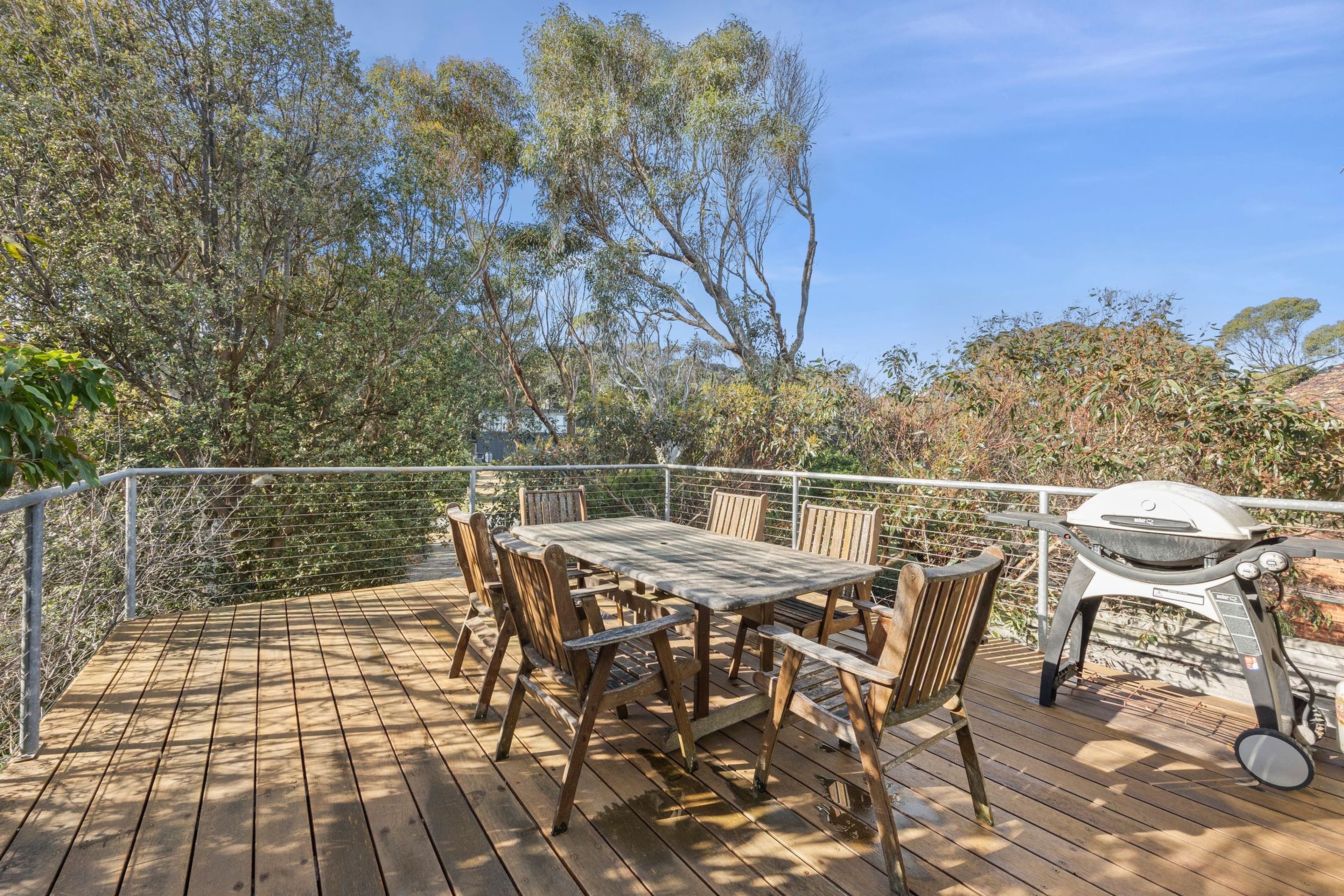 A wooden deck with a table and chairs, surrounded by a metal railing, and a barbecue grill.