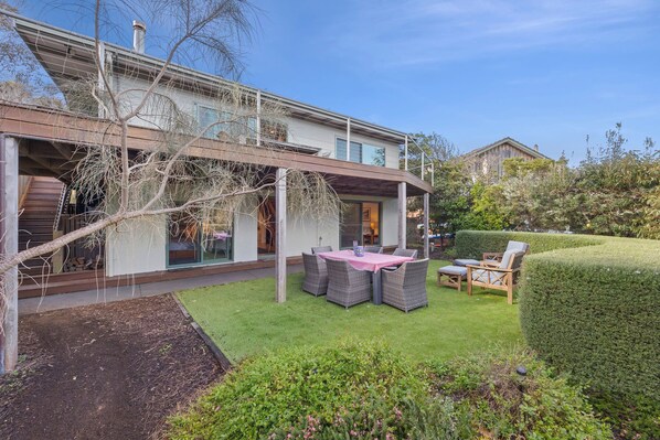 A modern house with a covered patio, a dining area with outdoor furniture, and a well-maintained garden.