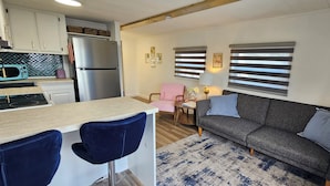 Un espacio habitable compacto con kitchenette, un sofá, una silla y una pequeña mesa con lámpara.