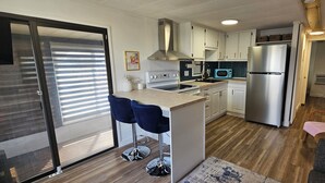 Una cocina moderna con un refrigerador de acero inoxidable, un microondas y una estufa a gas. Hay dos taburetes azules y un comedor de madera.