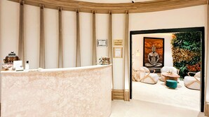 A reception area with a curved marble counter, a Buddha statue, and a green plant.
