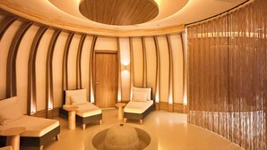 A modern spa room with a circular ceiling design, a central seating area, and a large window with curtains.