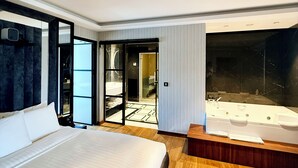 Una habitación de hotel moderna con una cama grande, una ba ñera y vistas a un paisaje urbano a través de amplios ventanales.