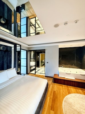 A modern hotel room with a large bed, a bathtub, and a view of a cityscape through large windows.