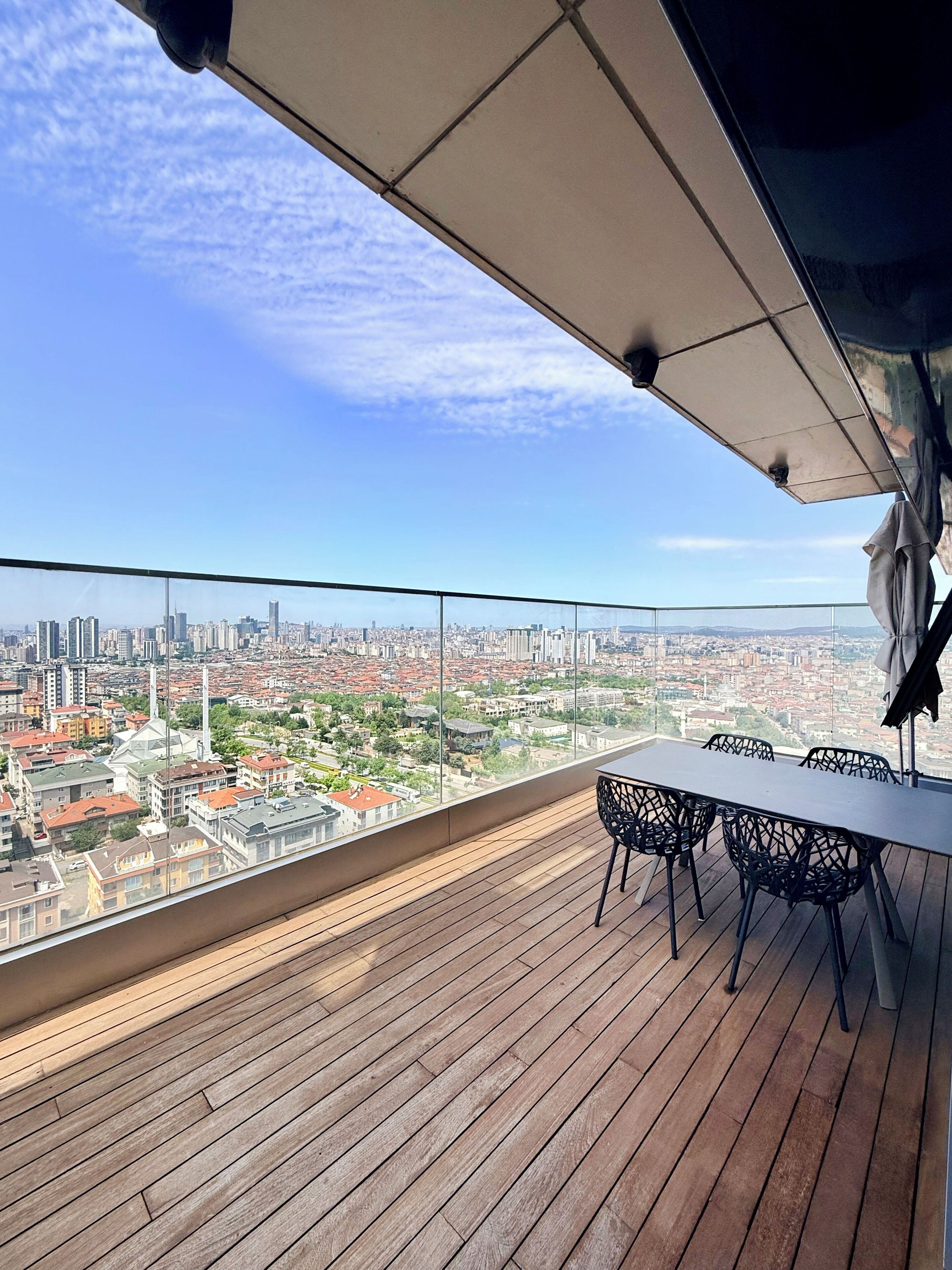 A rooftop terrace with a table and chairs, offering a panoramic city view.