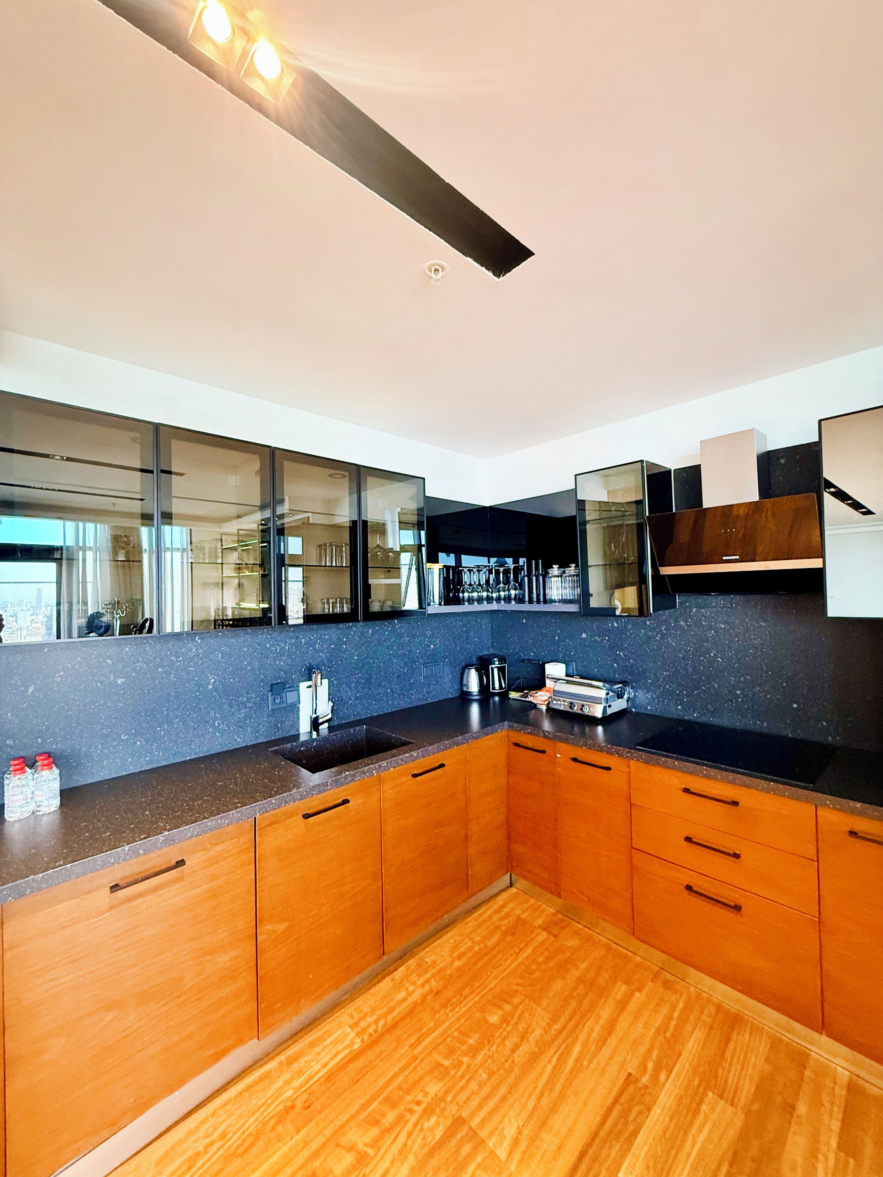 Een moderne keuken met houten kastjes, een zwart aanrecht en een RVS spoelbak.