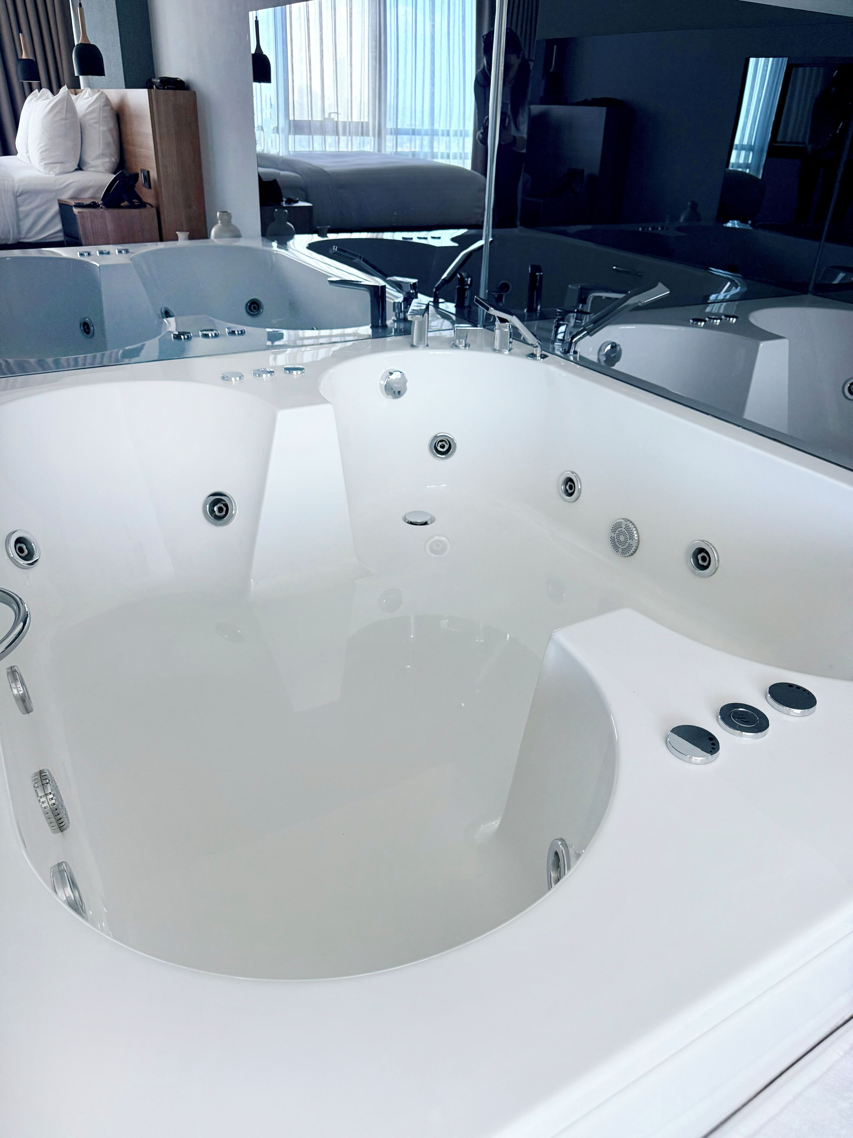A modern bathroom with a large bathtub, a mirror, and a window.