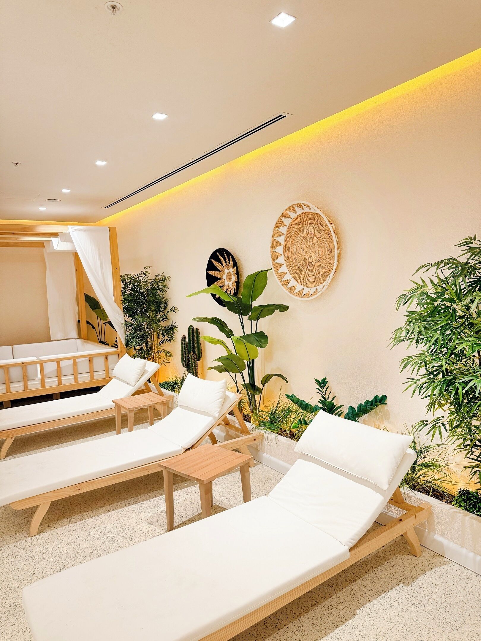A spa area with wooden loungers, a ceiling with recessed lighting, and various plants.