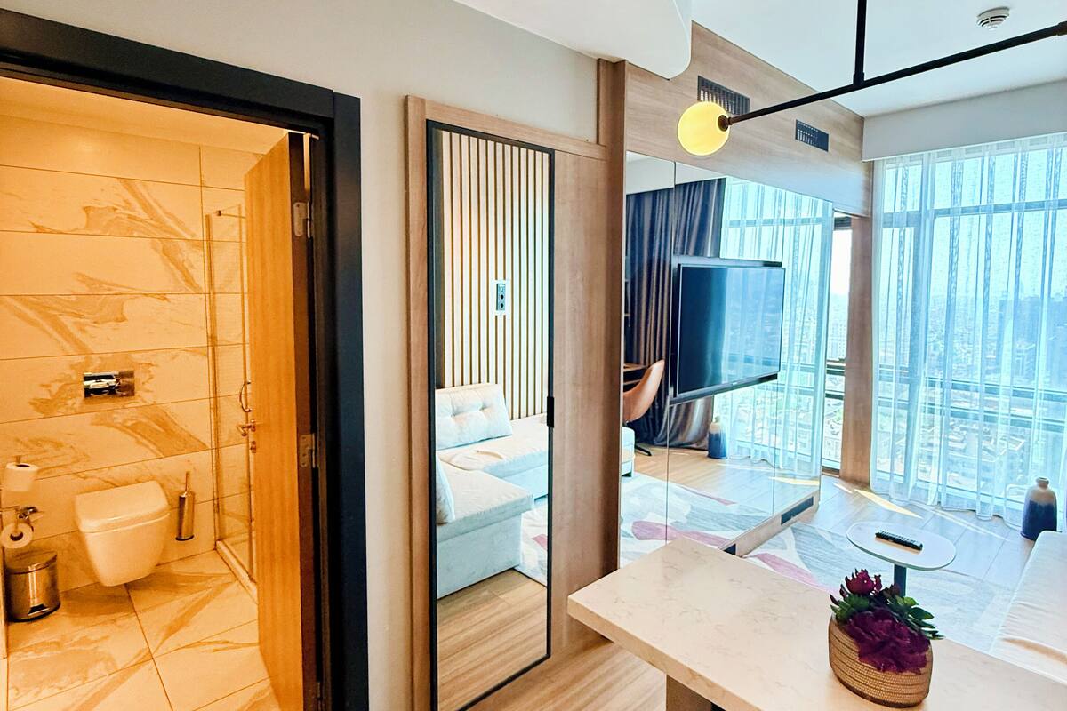 Ein modernes Hotelzimmer mit Bad, Essbereich und großem Fenster mit Blick auf die Stadt.