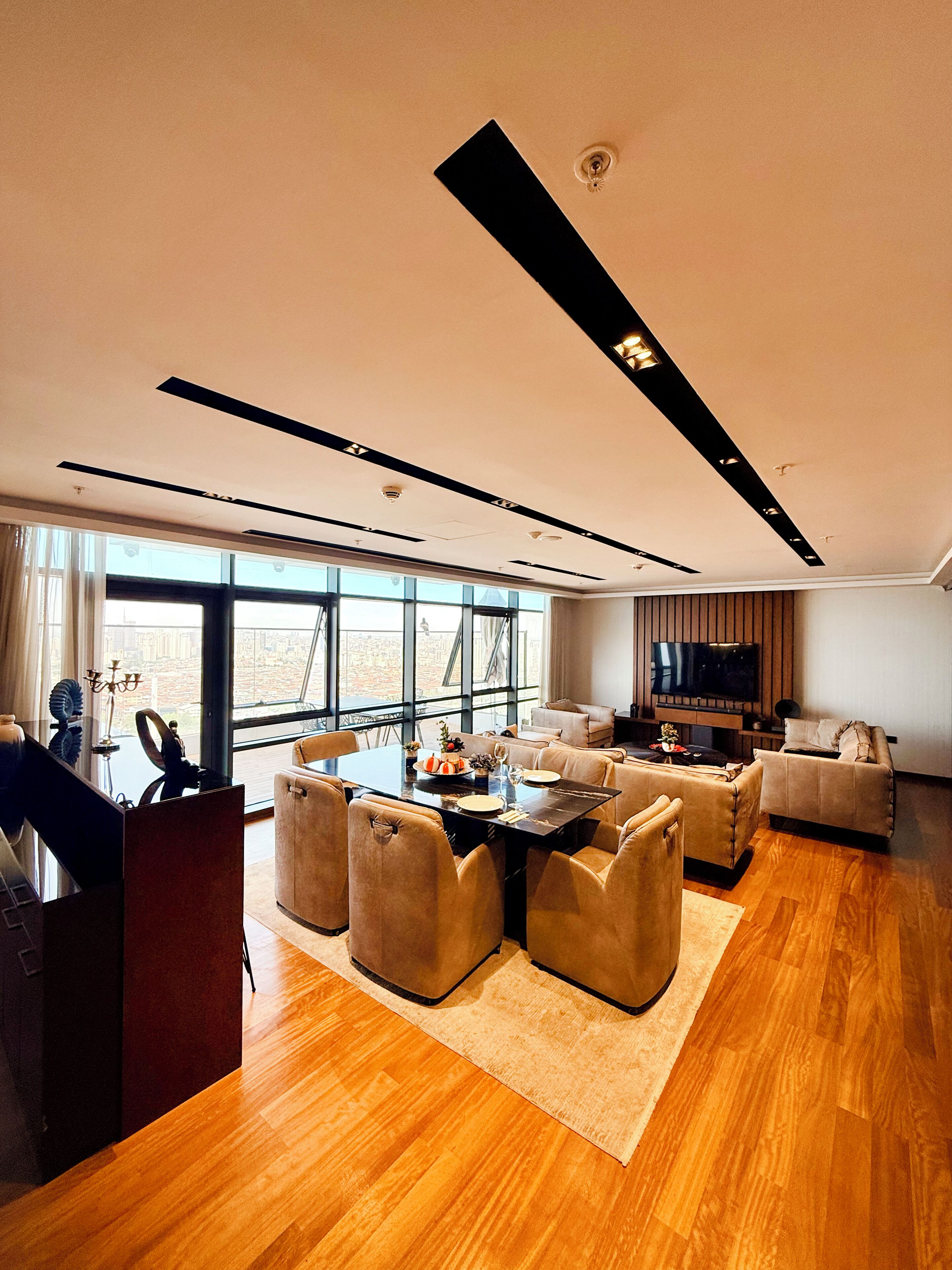 A modern living room with a dining area, large windows, and a flat-screen TV.