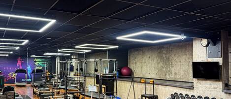 A gym with various exercise equipment, wooden flooring, and a ceiling with grid-like lighting fixtures.
