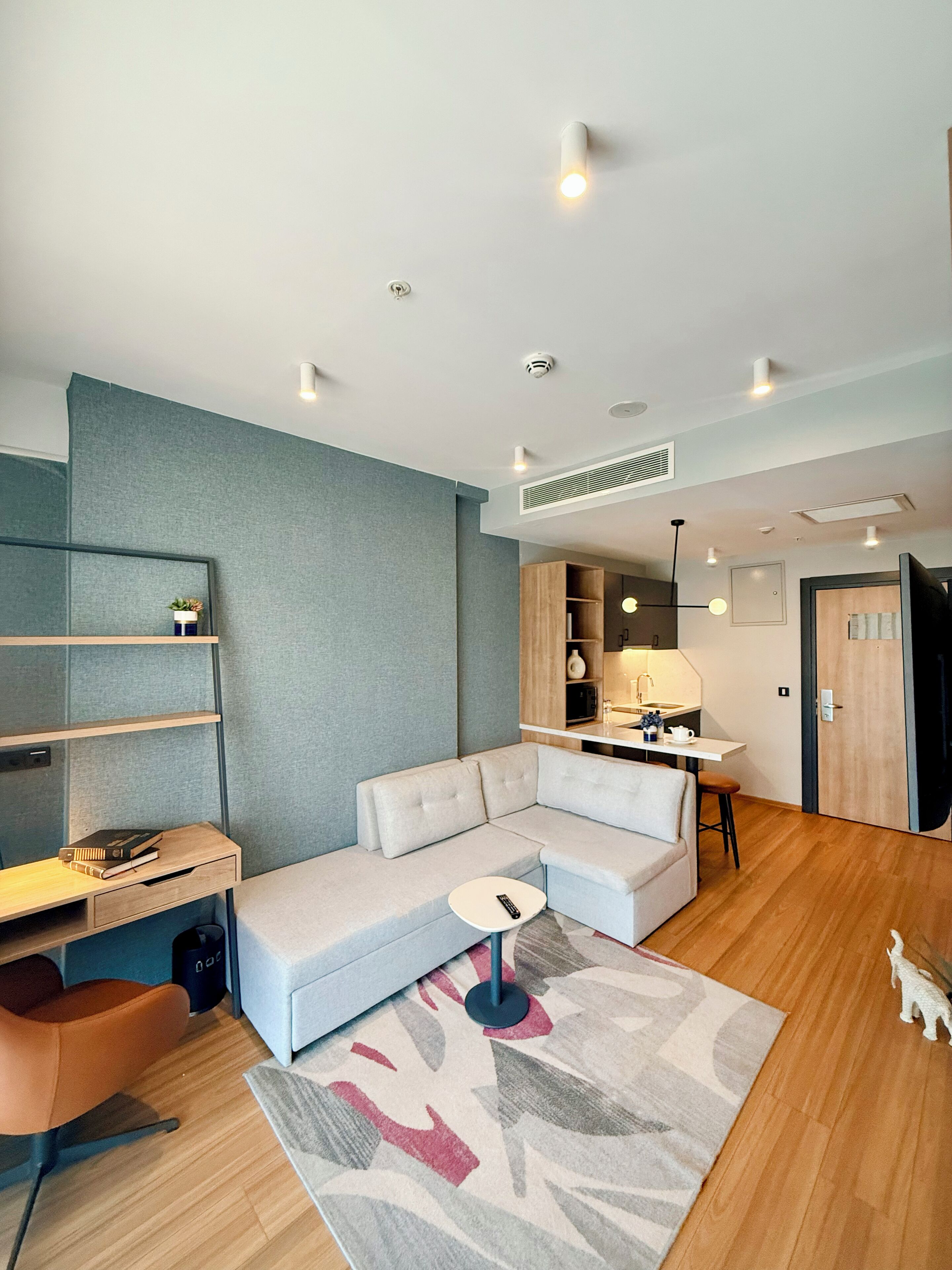Een moderne woonkamer met een modulaire bank, een kleine tafel, een bureau met stoel, een keukenhoek en een deur.
