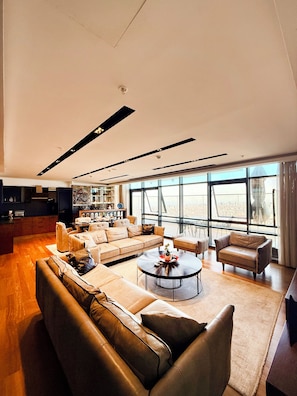 A spacious living area with a large sofa, a coffee table, and a view of the city through large windows.