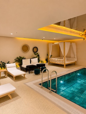 Area piscina interna moderna con un letto, sedie a sdraio e un tavolino.