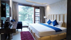 Una habitación de hotel con una cama, un escritorio con cafetera, una silla, un televisor y vistas a árboles por la ventana.