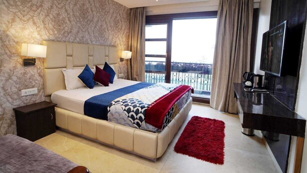 Habitación de hotel moderna con una cama grande, televisión, vistas al balcón y una alfombra roja.