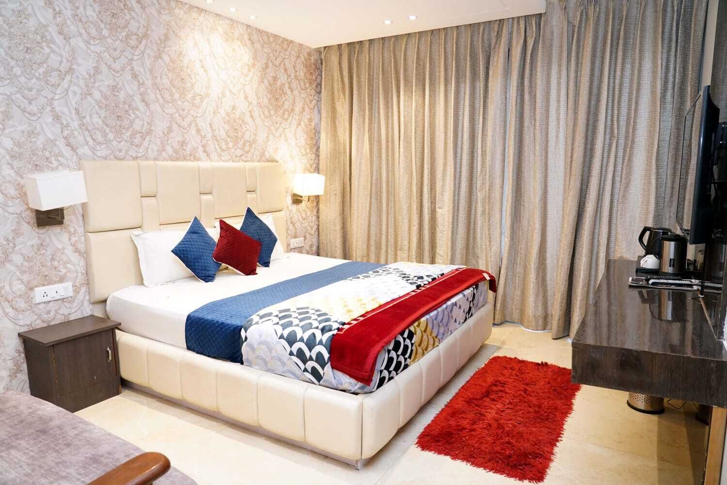 A hotel room with a bed, bedside table, lamp, curtains, and a coffee maker.