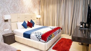 Una habitación de hotel con cama, mesita de noche, lámpara, cortinas y cafetera.
