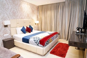 Una habitación de hotel con cama, mesita de noche, lámpara, cortinas y cafetera.