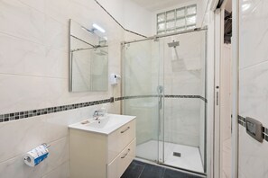 Ein Badezimmer mit Duschkabine, Waschbecken mit Spiegel und Toilettenpapierhalter.
