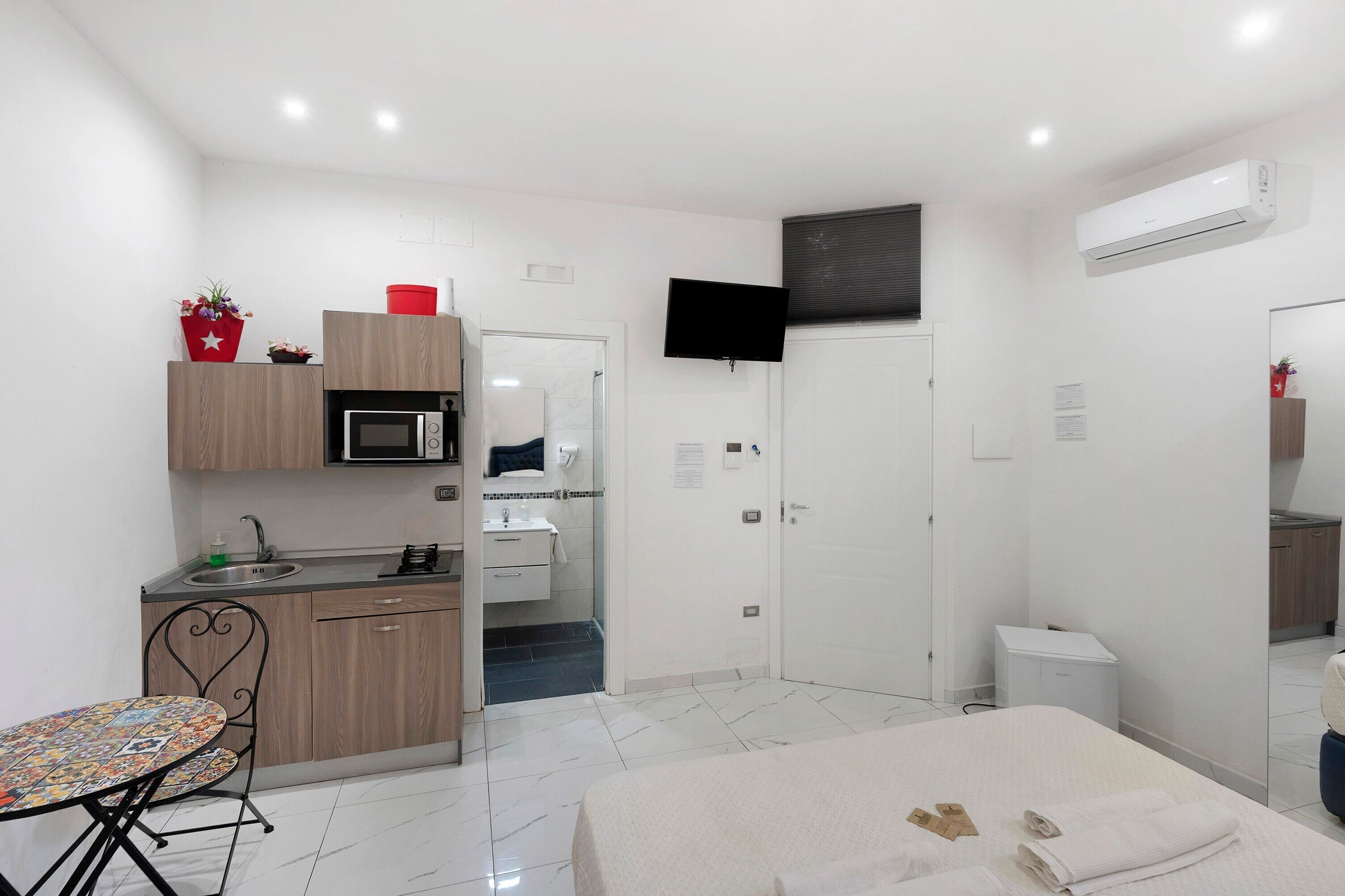 A modern, well-lit room with a kitchenette, a dining area, and a bed.