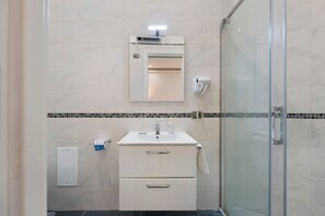 A bathroom with a glass shower enclosure, a white sink with a mirror above it, and a towel hanging on the wall. - Standard Studio Apartment with Wi-Fi and Air Conditioning (Salerno)