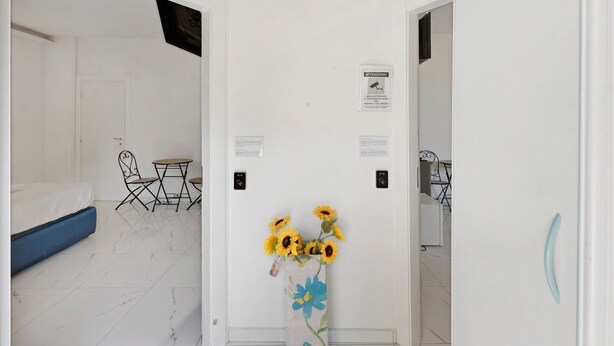A hotel room with a bed, a small table with chairs, a vase with sunflowers, and a door with a sign. - Standard Studio Apartment with Wi-Fi and Air Conditioning (Salerno)