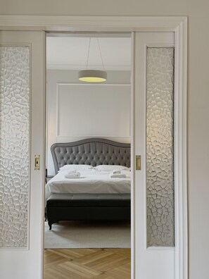 A bedroom with a tufted headboard, a bed with white linens, a hanging light fixture, and textured wall panels. - Athens Acropolis View Balcony 2 Min to Metro (Athina)