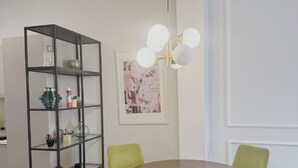 En matplats med ett runt bord, gröna stolar, en svart hylla och en väggmonterad lampa.