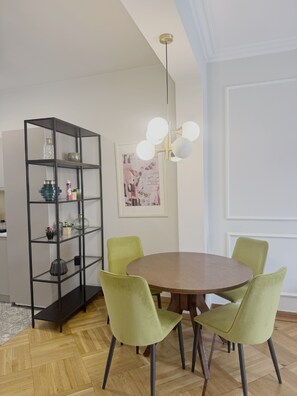 A dining area with a round table, green chairs, a black shelving unit, and a wall-mounted light fixture. - Athens Acropolis View Balcony 2 Min to Metro (Athina)
