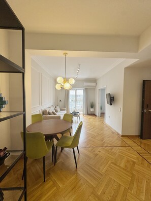 A spacious living area with a wooden herringbone floor, a round dining table with chairs, a sofa, and a modern chandelier. - Athens Acropolis View Balcony 2 Min to Metro (Athina)