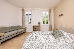 Une chambre à coucher comprenant un lit, un canapé, deux fenêtres, une table de chevet et un radiateur.