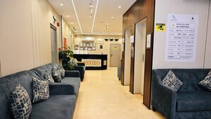 A hotel reception area with a reception desk, two sofas with patterned cushions, a plant, and a wall-mounted information board. - Sari Almisk Hotel (Makkah)