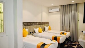 A hotel room with three beds, an air conditioning unit, a patterned headboard, and a window with curtains. - Sari Almisk Hotel (Makkah)