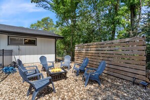 A patio with Adirondack chairs, a fire pit, and a wooden fence. - Swimming Pool, Hot Tub, Bike-In/Out, Fire Pit, Ping Pong and Snow Cone Machine (Bentonville)