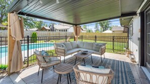 Un porche cubierto con mobiliario exterior, piscina y vista al jardín trasero.