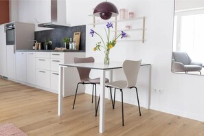 A modern kitchen with white cabinetry, a dining table with chairs, a pendant light, and a vase with flowers. - To Koje... (Sankt Peter-Ording)