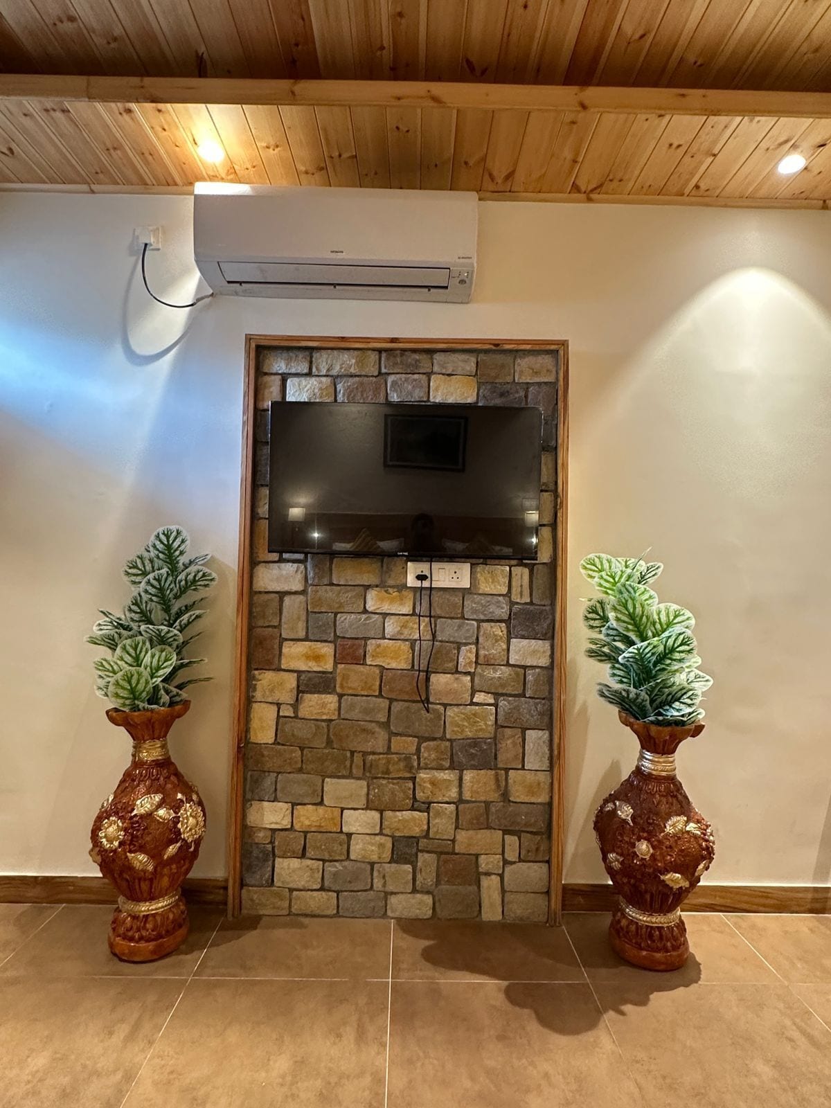Una habitación con pared de piedra, un televisor de pantalla plana y dos jarrones decorativos.