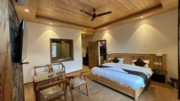 A bedroom with a wooden ceiling, a bed with white bedding, a wooden desk with a chair, and a television mounted on the wall.