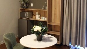 A hotel room with a round table, two chairs, a TV, a wooden shelf, and a grey curtain. - Stay Local Potchefstroom (Potcherfstroom)