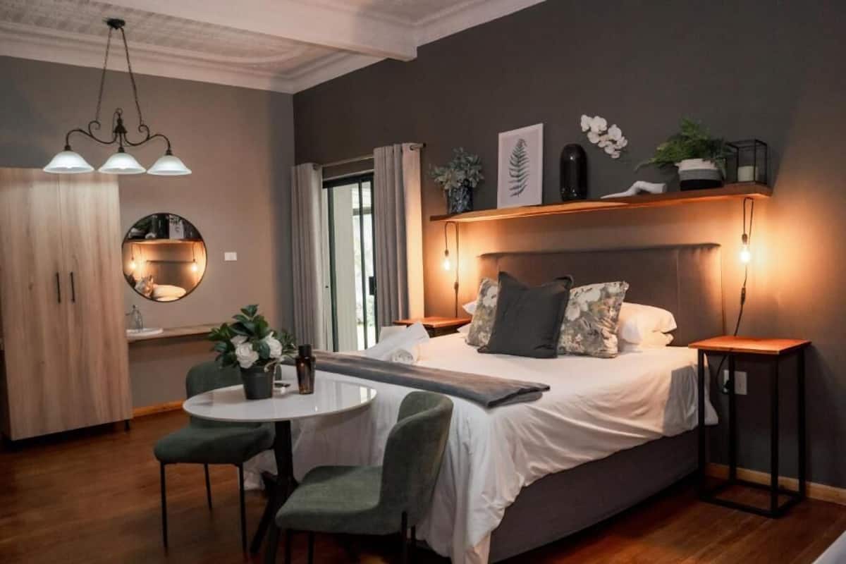 A modern bedroom with a bed, bedside tables, a round mirror, a small table with chairs, and a view of the outside.