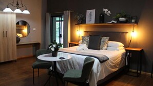 A hotel room with a bed, two bedside tables, a round table with chairs, a mirror, and a wardrobe. - Stay Local Potchefstroom (Potcherfstroom)
