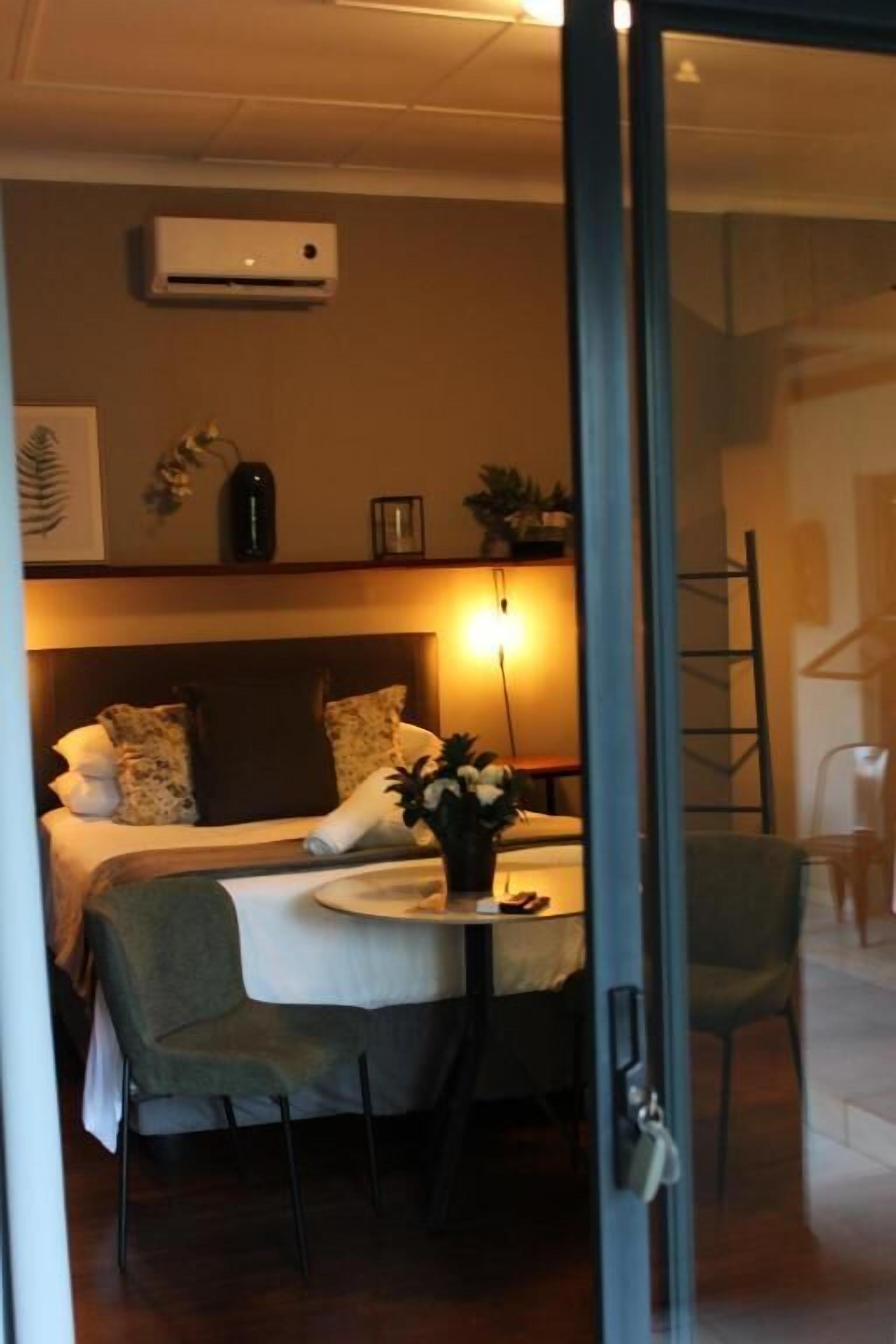 Une chambre d’hôtel avec un lit, une table de chevet, une chaise et une petite table sur laquelle se trouve un vase de fleurs.
