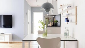 Eine moderne Küche mit Flachbildfernseher, Esstisch mit Stühlen, einer hängenden Pendelleuchte und eingebauten Regalen mit Geschirr.