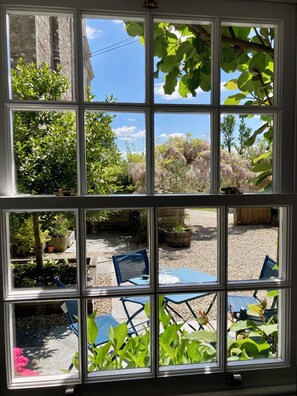 Ein Fenster mit Blick auf einen Garten, Sitzgelegenheiten im Freien und ein Gebäude im Hintergrund.