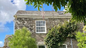 A stone building with a green door, two windows, and a garden with chairs. - Laundry Cottage: a little piece of heaven in North Cornwall! (Bodmin)