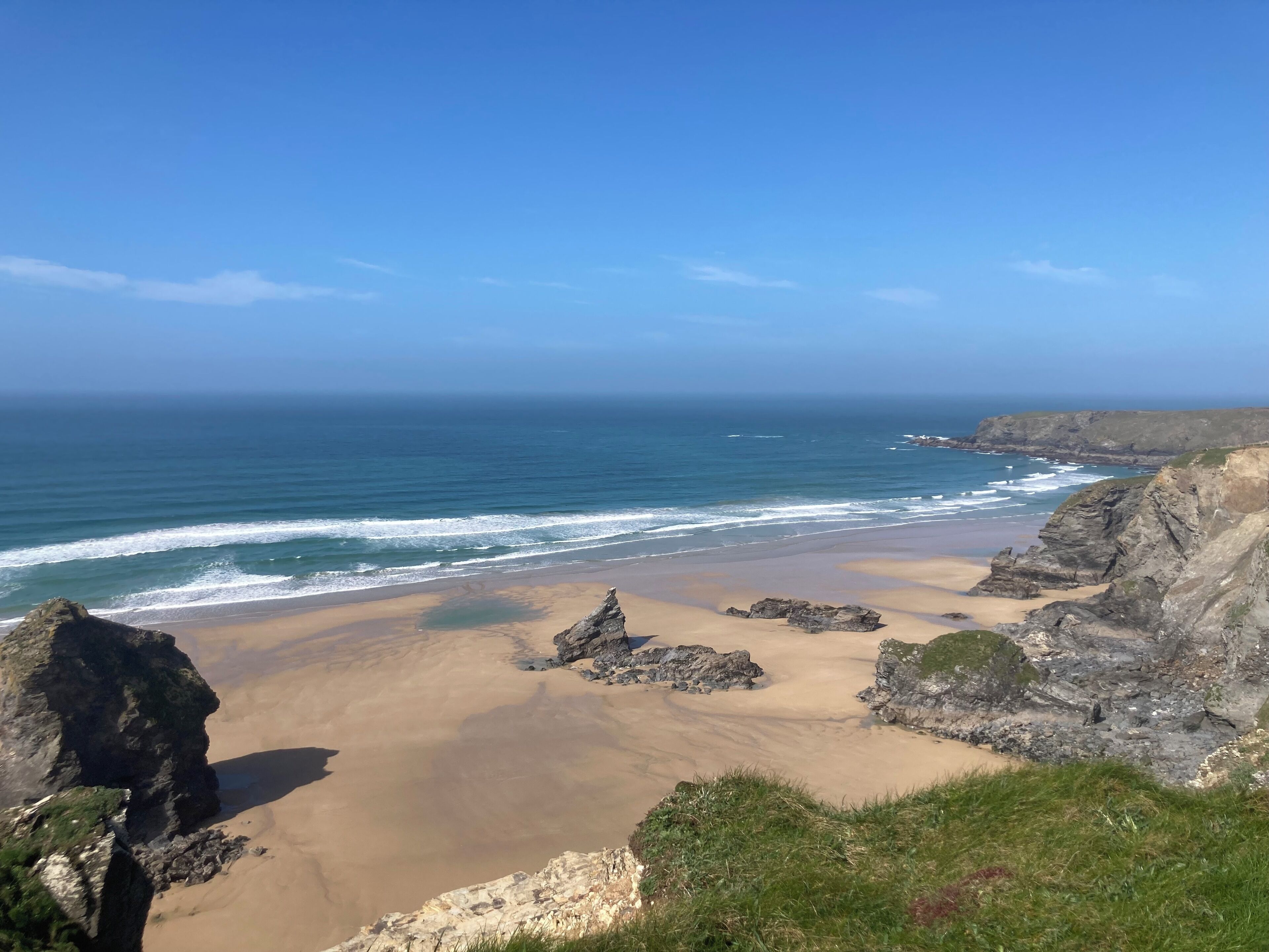 A coastal landscape with a sandy beach, rocky cliffs, and the ocean.