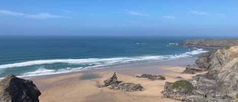 A coastal landscape with a sandy beach, rocky cliffs, and the ocean.