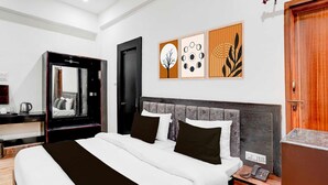 A modern hotel room with a large bed, a bedside table with a phone, a mirror, and artwork on the wall. - Townhouse Sarnath Temple (Varanasi)