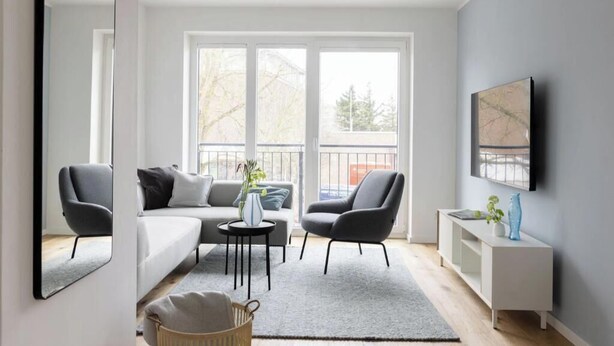 Ein modernes Wohnzimmer mit einer Couch, zwei Sesseln, einem Couchtisch, einem Beistelltisch und einem an der Wand befestigten Fernseher.